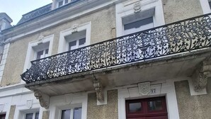 A building with a red door, white-framed windows, and a decorative metal balcony railing.