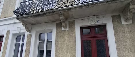 Un bâtiment avec une porte rouge, des fenêtres à cadre blanc et un balcon orné d’une balustrade en métal.