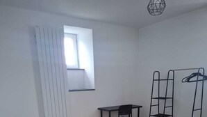 A bedroom with a bed, a desk, a chair, a radiator, and a window.