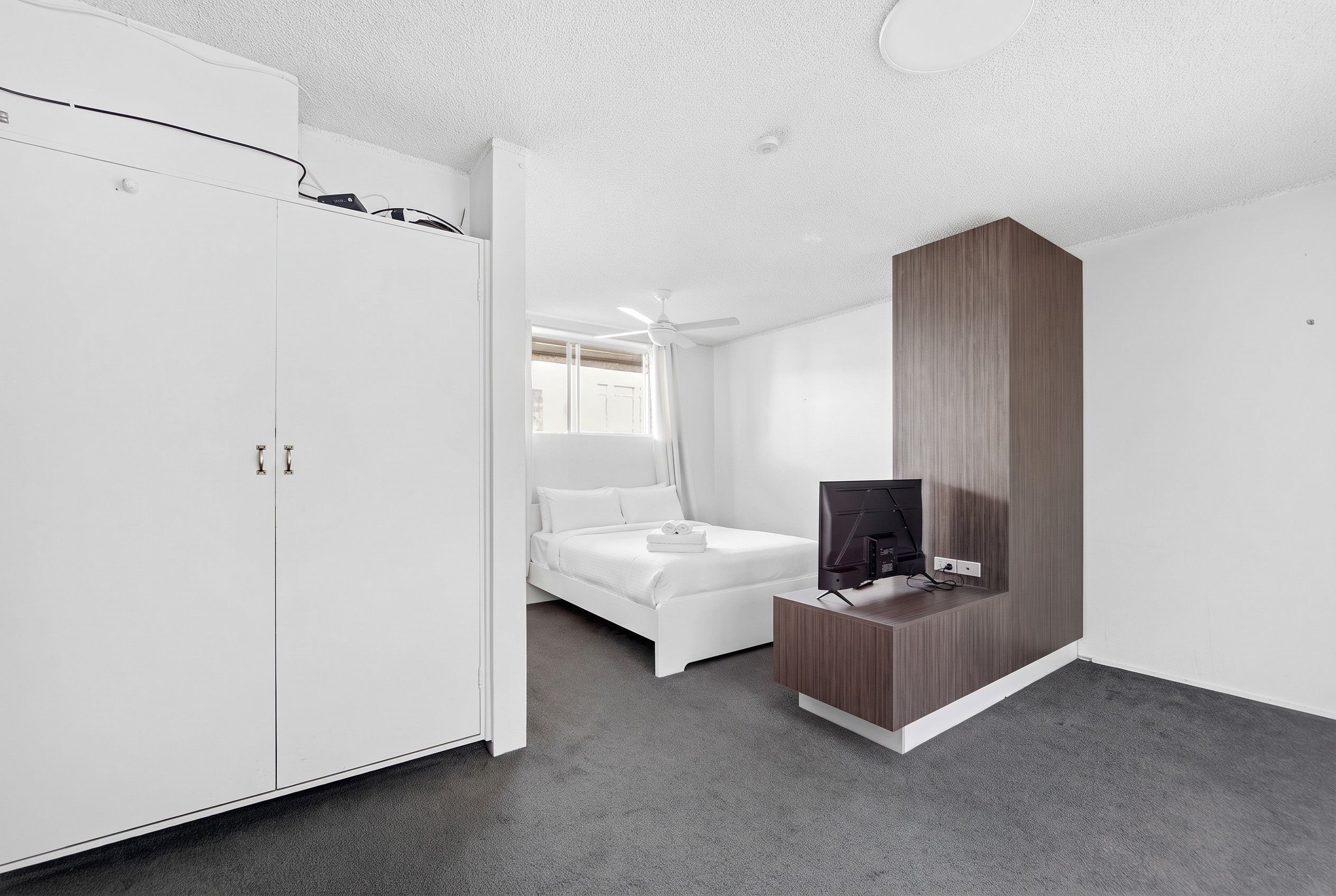 Et moderne soveværelse med seng, garderobe, fjernsyn og loftventilator.