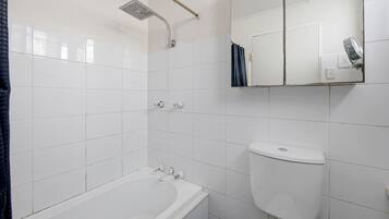 Ein Badezimmer mit einer weißen Badewanne, einer Duschbrause, einer Toilette und einem Spiegel.