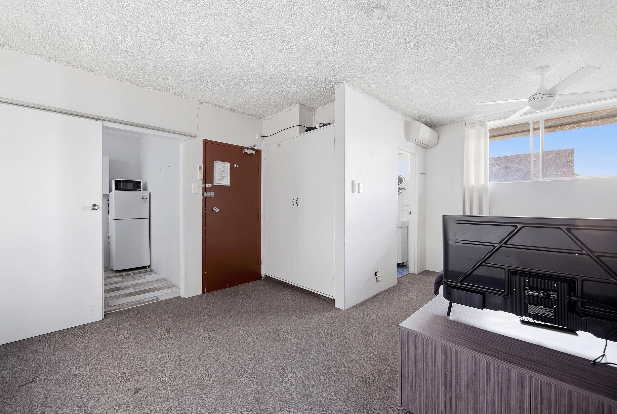 A hotel room with a kitchenette, a wardrobe, a television, and a view of the outdoors.