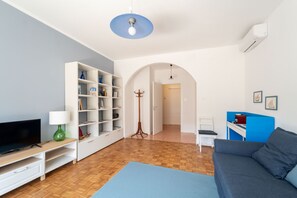 A living room with a television, bookshelf, sofa, and a blue mat on the floor. - A comfortable and welcoming 50 square meters apartment, perfect for four people, located on the sixth floor of a building with an elevator (NOT accessible to people with disabilities).The property is situated in a quiet area not far from the center of Tr (Trieste)