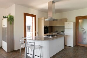 Cozinha moderna com ilha central, eletrodomésticos de aço inoxidável e vista para o exterior.