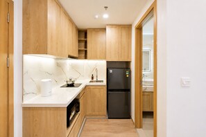 A compact kitchen with wooden cabinets, a black refrigerator, a built-in oven, and a marble backsplash. - Nice apartment with AC in vibrant Hà Nội city center (Hà Nội)