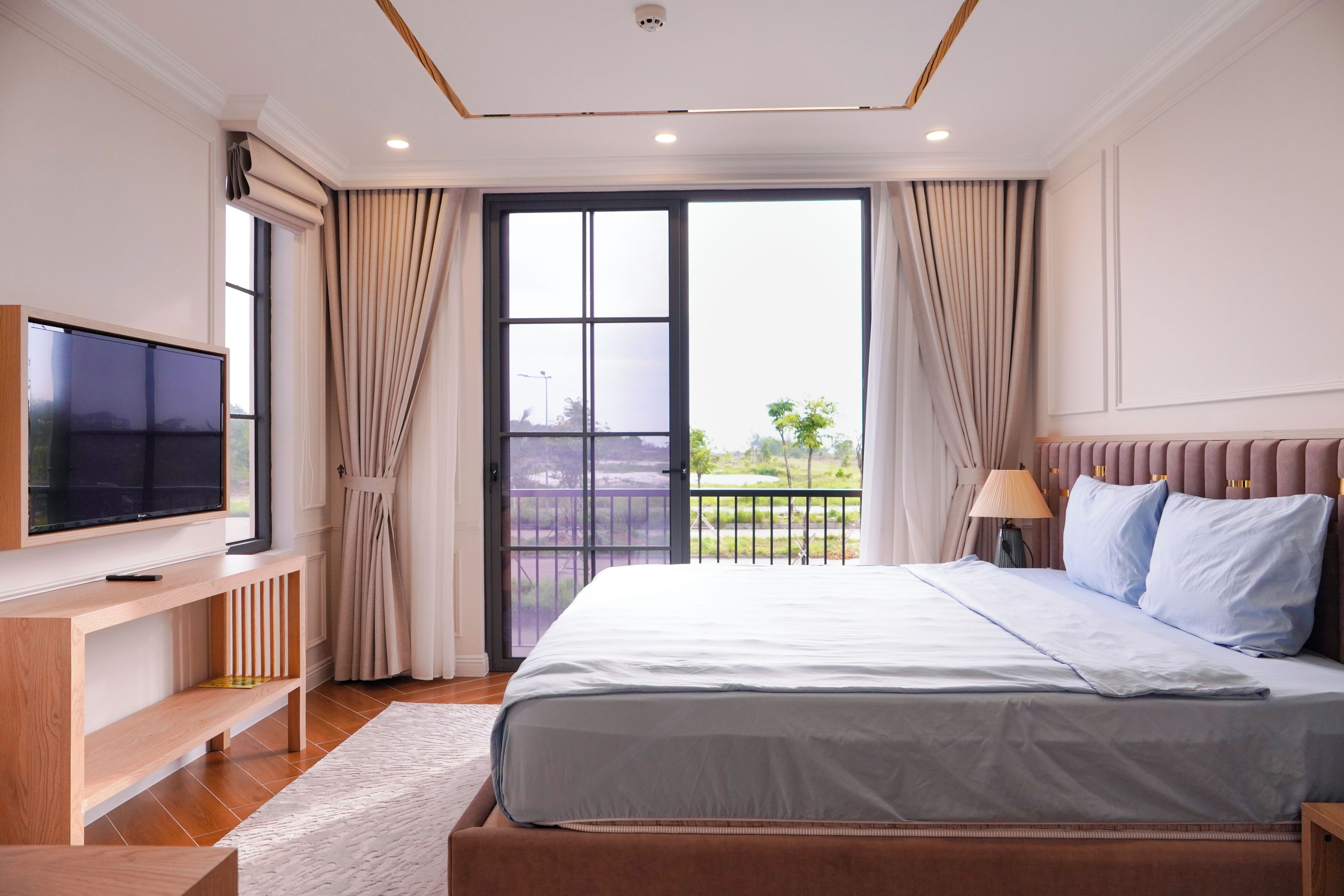 A bedroom with a bed, a TV, a desk, and a balcony with curtains.