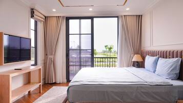 A bedroom with a bed, a TV, a desk, and a balcony with curtains.