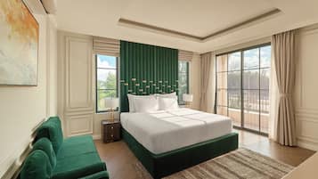 A spacious bedroom with a large bed, a green accent wall, and a view of the outdoors through a large window.