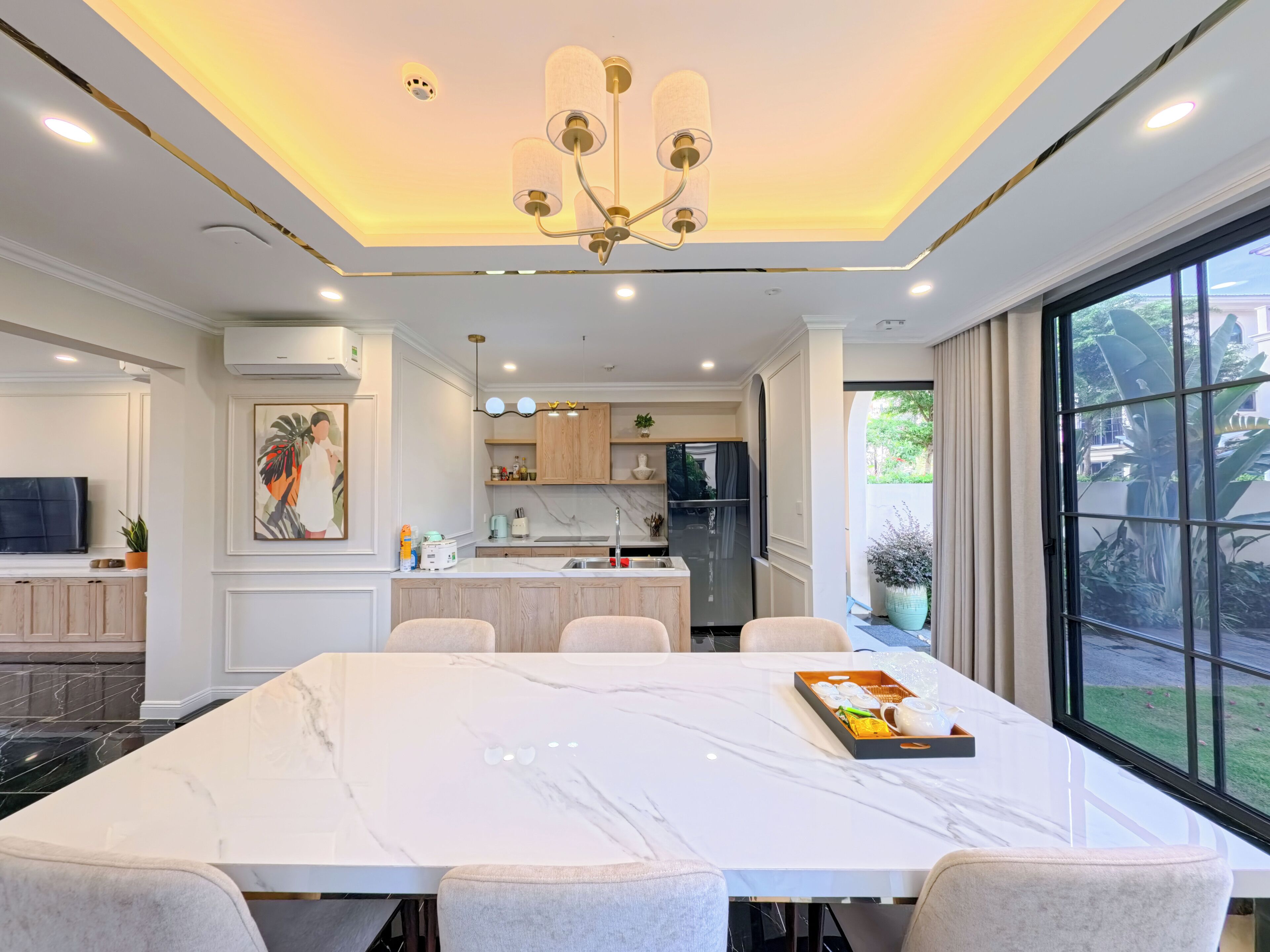 A modern kitchen with a marble countertop, a dining area with a large table, and a view of the outdoors through a large window.