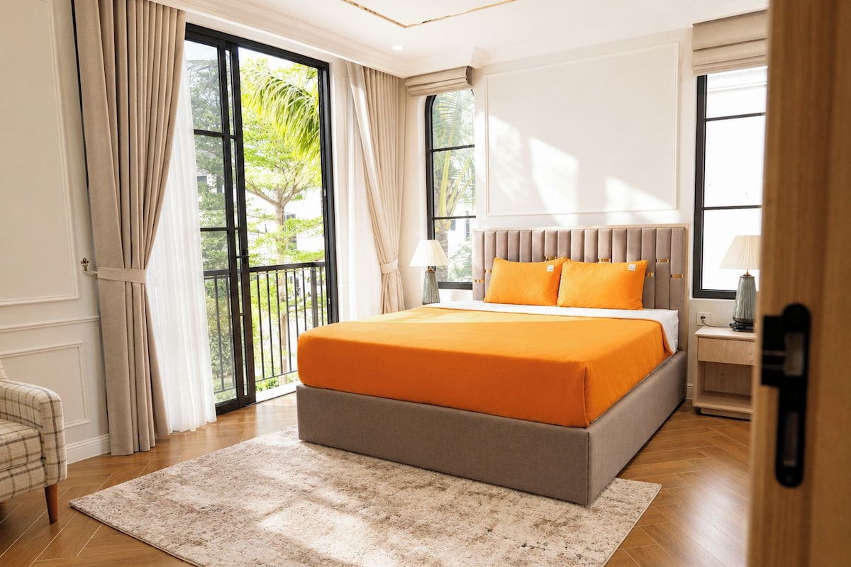 A hotel room with a large bed, a view of greenery through the windows, and a balcony.