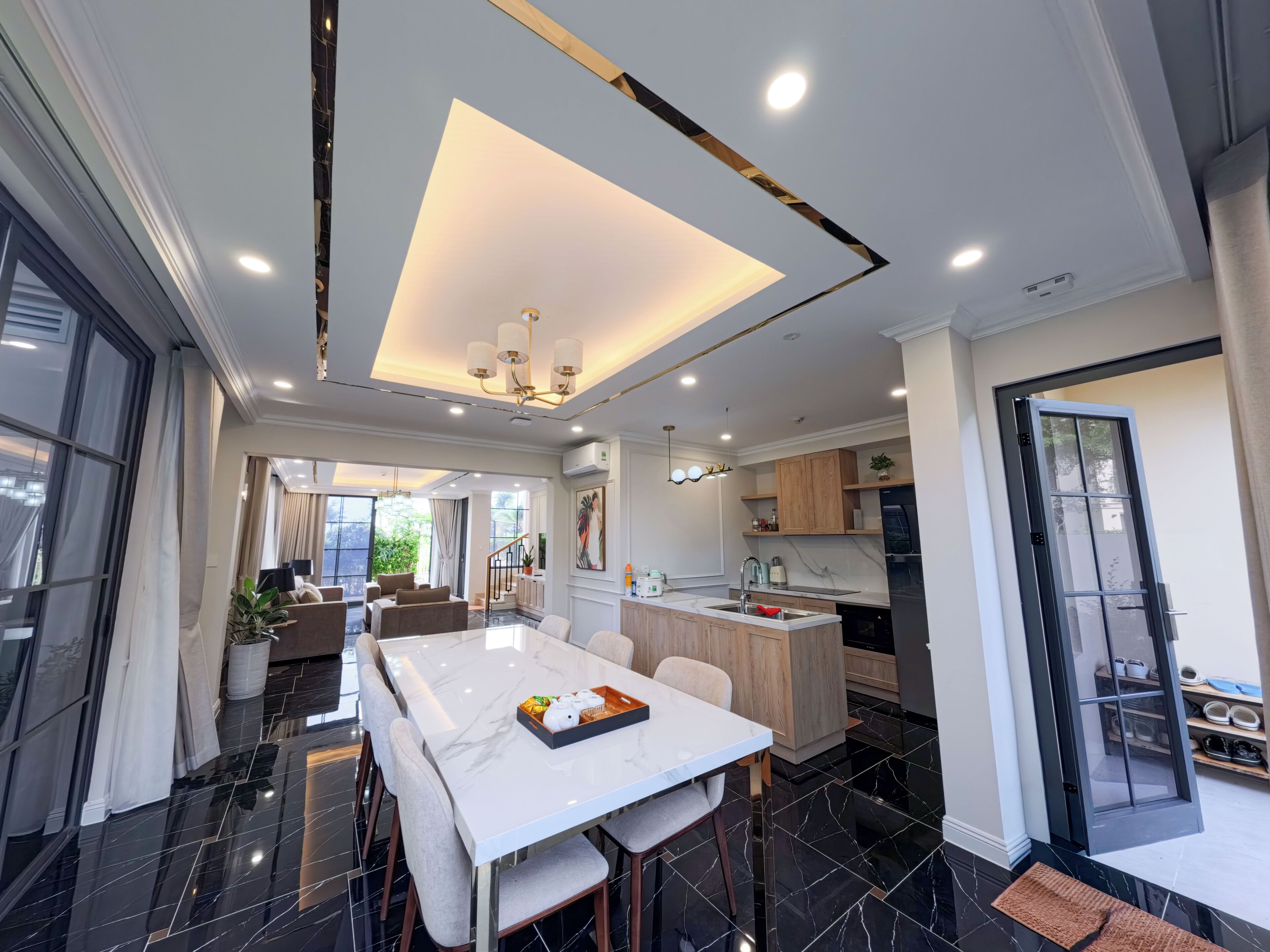 A modern kitchen with a central island, a dining area with a marble table, and a view of the outdoors.