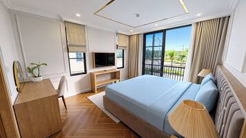 A modern hotel room with a large bed, a TV, a desk, and a balcony with a view.