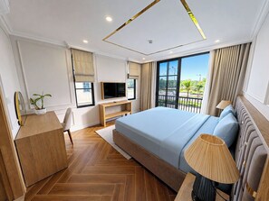 A modern hotel room with a large bed, a TV, a desk, and a balcony with a view. - Sonasea Villas Collection Residence (Duong To)
