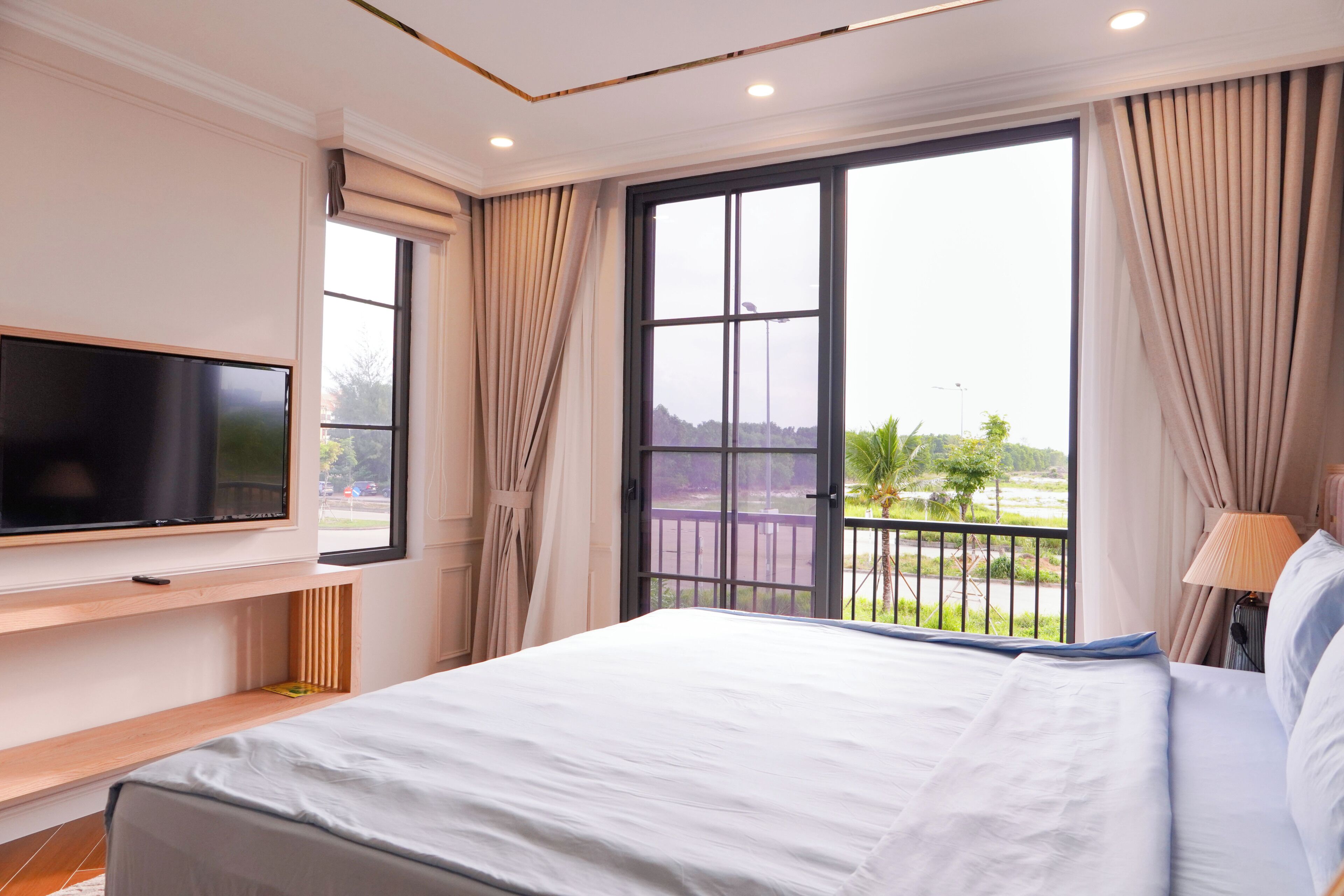 A hotel room with a bed, a TV mounted on the wall, and a balcony with a view of the outdoors.