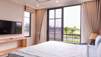 A hotel room with a bed, a TV mounted on the wall, and a balcony with a view of the outdoors.