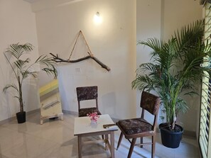 Una habitación con una mesa blanca, dos sillas, una rama decorativa en la pared y plantas en macetas.