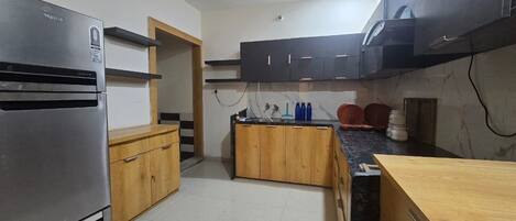 A kitchen with a refrigerator, wooden cabinets, a countertop, and a ceiling fan.