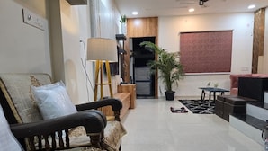 A modern living room with a sofa, a coffee table, a lamp, a potted plant, and a sliding door leading to a staircase. - The white Town Homestay (Indore)