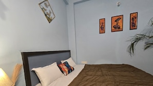 A hotel room with a bed, a nightstand, a lamp, and wall art. - The white Town Homestay (Indore)