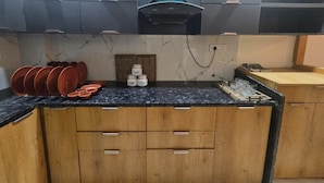 A kitchen with wooden cabinets, a black countertop, and a range hood above. - The white Town Homestay (Indore)
