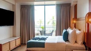 A hotel room with a bed, a TV, a balcony with a view of palm trees, and an air conditioning unit.