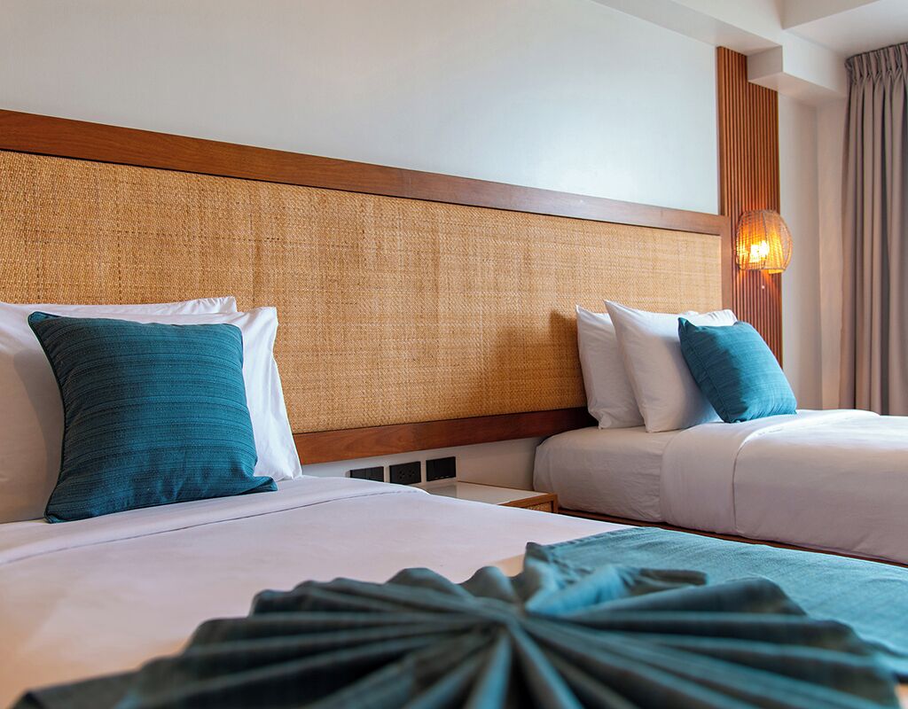 A hotel room with two beds, a woven headboard, and a bedside lamp.