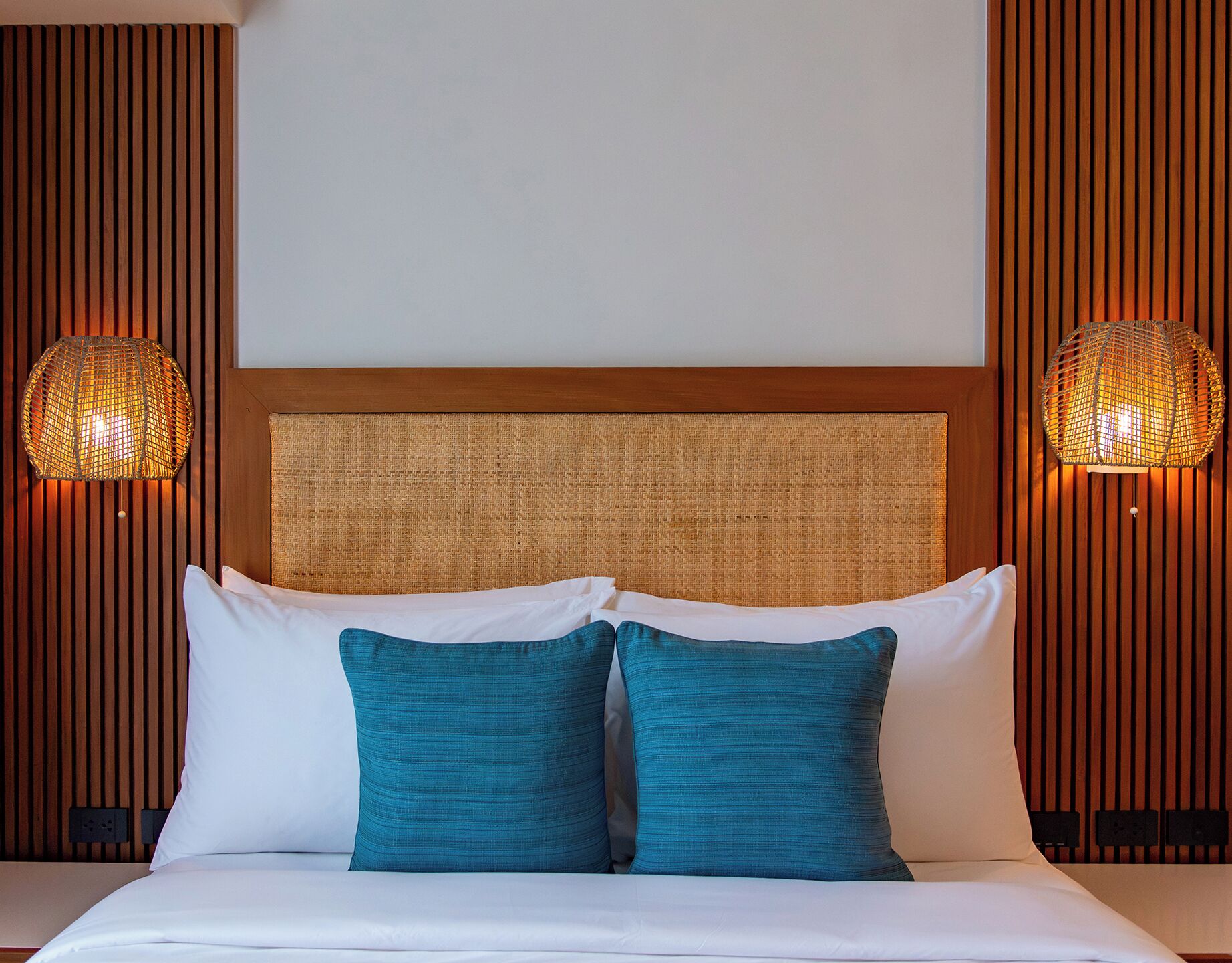Une chambre d’hôtel avec un lit, deux lampes fixées au mur et une tête de lit texturée.