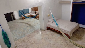 A room with a bed, a hammock, and a mop leaning against the wall.