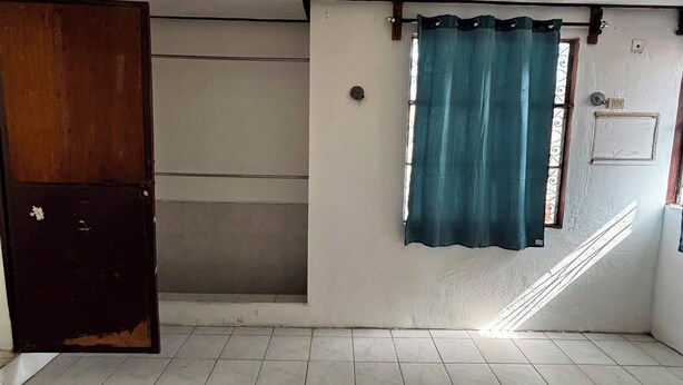 Habitación con ventilador de techo, ventana con cortinas, puerta y suelo de baldosas.