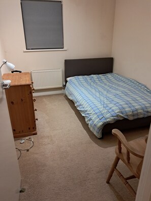 A bedroom with a bed, a wooden dresser, a desk with a lamp, and a radiator. - Family-sized holiday flat near the Surrey Hills and London (LEATHERHEAD)