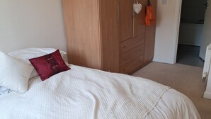 Un letto con biancheria bianca e un cuscino rosso, un armadio in legno e un termosifone bianco in una stanza.