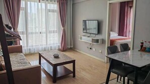A modern living room with a sofa, a coffee table, a TV mounted on the wall, and a dining area with chairs. - Hongdou Hotel Apartment (Dalian South China Yihecheng Branch) (Dalian)