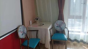 A room with a table, two chairs, a projector screen, and a window with curtains. - Hongdou Hotel Apartment (Dalian South China Yihecheng Branch) (Dalian)