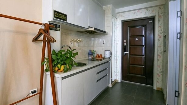 A compact kitchen with white cabinets, a stainless steel sink, and a wooden hanging rack. - Hongdou Hotel Apartment (Dalian South China Yihecheng Branch) (Dalian)