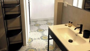 Un baño con lavamanos, espejo y estantería negra.