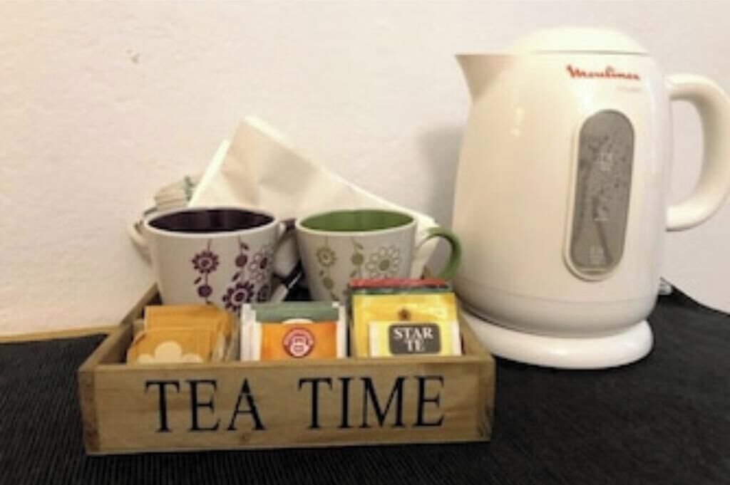 Een houten doosje met de tekst 'TEA TIME', theezakjes en een witte elektrische waterkoker.