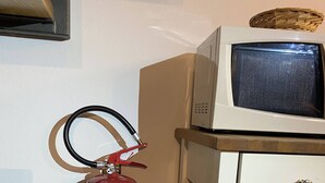 Ein an der Wand befestigter Feuerlöscher, ein Fernseher auf einem Holzbodenständchen und eine verzierte Schachtel auf einem Regal.