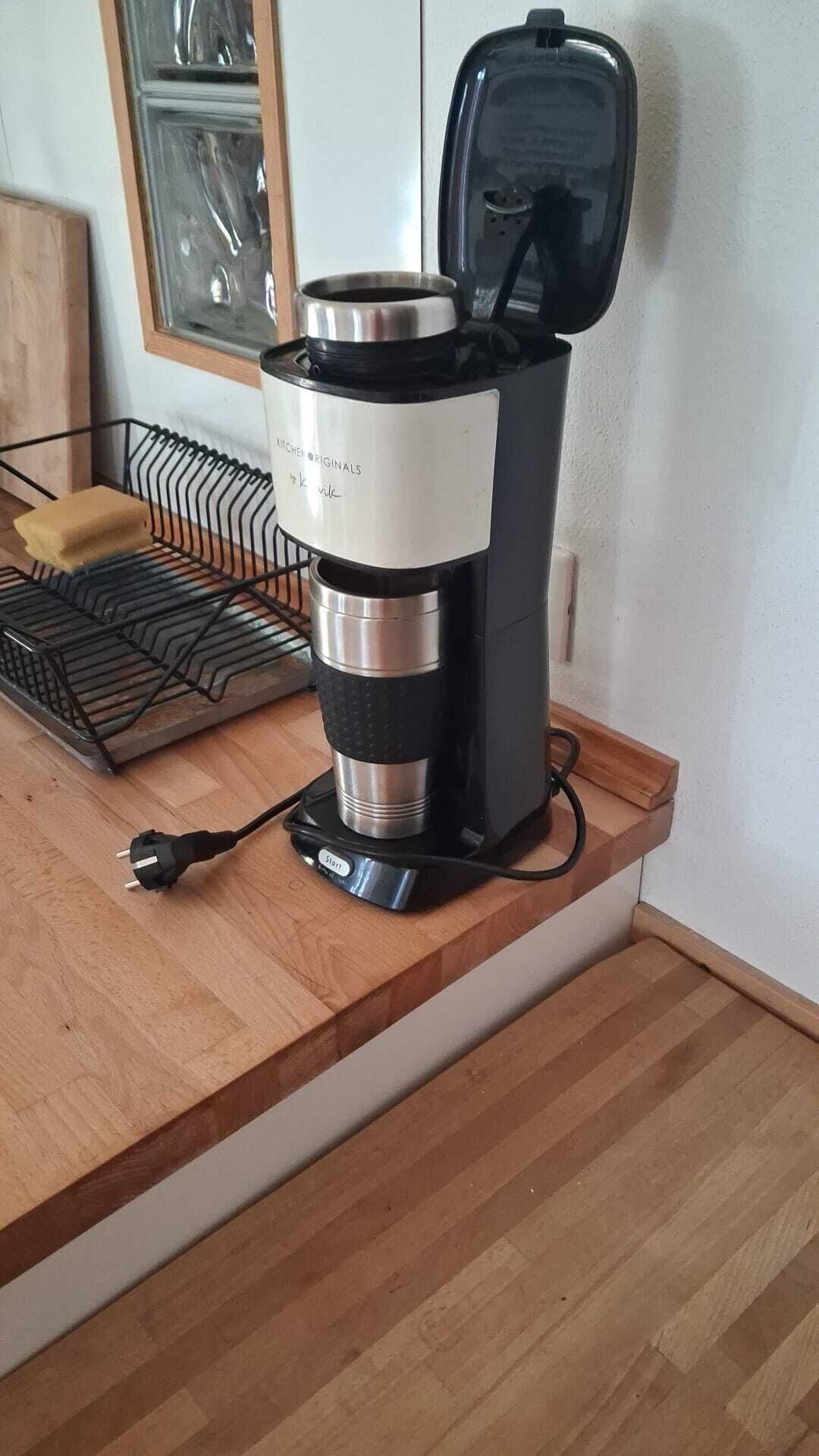 A coffee maker on a wooden countertop with a power cord plugged in.