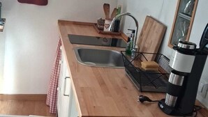 Eine kleine Küche mit einer Holzausziehtafel, einem Spülbecken, einer Kaffeemaschine und einem Regal mit verschiedenen Gegenständen.