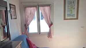A room with a bed, a dresser, a window with curtains, and a painting on the wall.