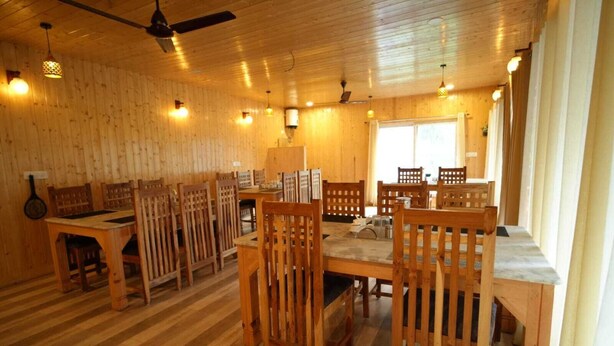 Un intérieur en bois avec plusieurs tables et chaises, des ventilateurs de plafond et des luminaires suspendus.