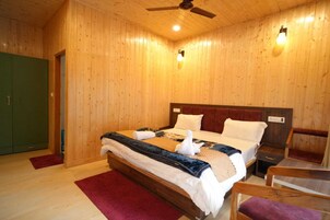 A wooden-paneled room with a bed, a nightstand, a chair, and a green door.