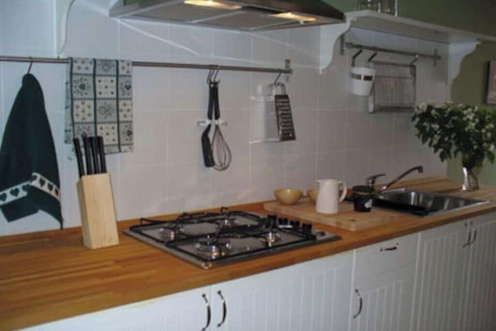 A kitchen with a gas stove, wooden countertop, white cabinets, hanging utensils, and a sink.