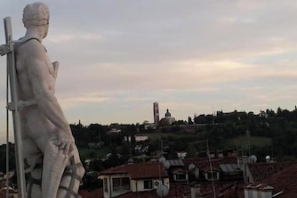 Eine Statue einer klassischen Figur, ein Gebäude mit rotem Dach und eine hügelige Landschaft im Hintergrund.