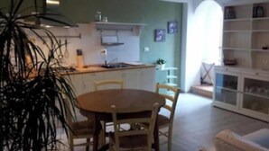 A dining area with a round table and chairs, a kitchen in the background, and a bookshelf to the right. - Bright apartment in the heart of Vicenza's historic center (Vicenza)