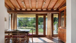 A room with a wooden ceiling, a dining table with chairs, a cabinet, and a view of a garden through glass doors. - Villa Il Rossignolo Apartment – Private Garden, Shared Pool & Terrace, Wi-Fi (Grassina)