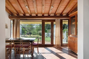 A room with a wooden ceiling, a dining table with chairs, a cabinet, and a view of a garden through glass doors. - Villa Il Rossignolo Apartment – Private Garden, Shared Pool & Terrace, Wi-Fi (Grassina)