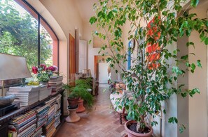 A cozy room with a large window, a bookshelf, a potted plant, and a door leading to another room. - Villa Il Rossignolo Apartment – Private Garden, Shared Pool & Terrace, Wi-Fi (Grassina)