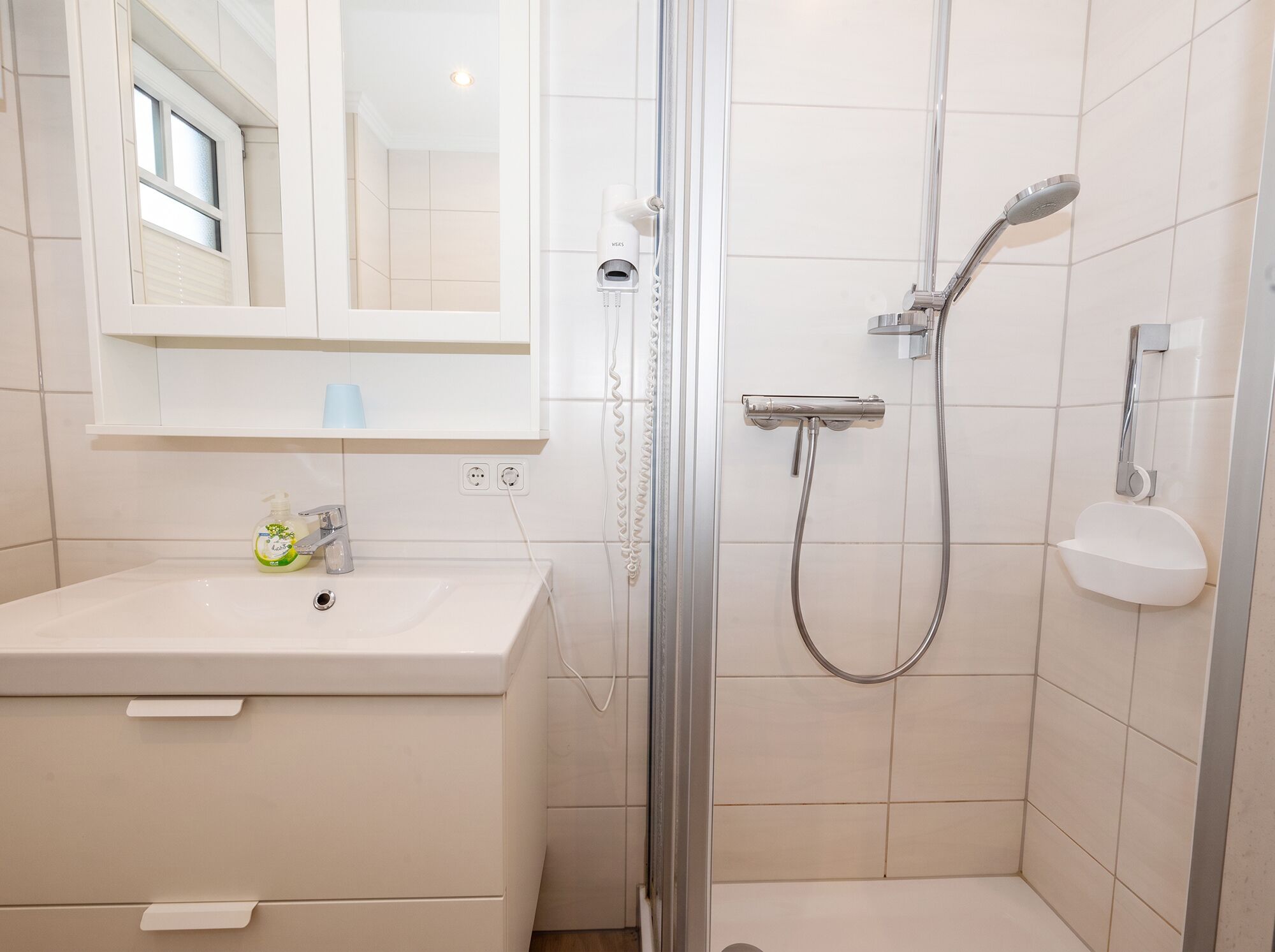 A bathroom with a glass-enclosed shower, a white sink, and a mirror above the sink.