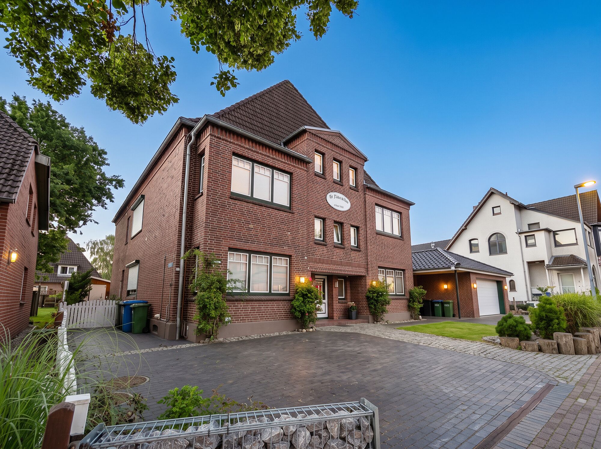 A two-story brick house with a garage, surrounded by a paved driveway and greenery.